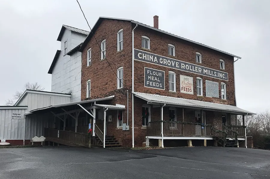 The three-story brick China Grove Roller Mill with painted signs reading China Grove Roller Mills and Flour Meal Feeds, and a covered wooden porch